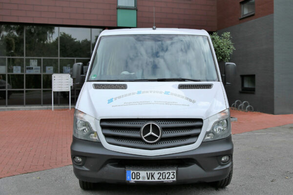 Ein weißer Mercedes Transporter steht vor einem Gebäude mit roter Ziegelmauer. Auf der Windschutzscheibe und den Seitentüren des Fahrzeugs ist Werbung für eHygiene-Service-Kegenhof angebracht, das Hygieneartikel, Aircare-Geräte und Spendersysteme für Desinfektionsmittel anbietet. Im Hintergrund spiegeln sich Bäume und der Himmel in den Fenstern des Gebäudes.